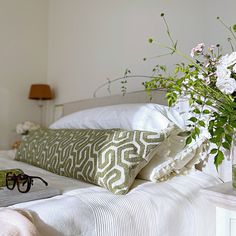 a white bed topped with pillows and a vase filled with flowers