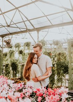 a man and woman standing next to each other in a greenhouse with pink flowers on the ground