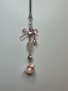 a hello kitty keychain hanging from a hook on a white wall with a red bow