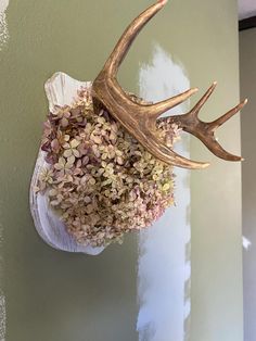 a deer's head hanging from the side of a wall with flowers in it