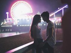 a man and woman standing next to each other in front of a ferris wheel at night