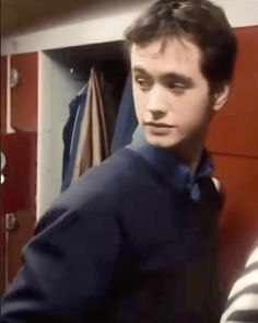 a young man standing in front of a red locker with his hand on his hip