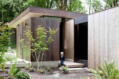 a little boy standing in front of a building with trees and plants around it on the side