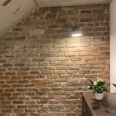 a room with a brick wall and wooden table in the corner, next to a lamp