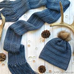 a knitted hat, scarf and antlers on a white wooden table with pine cones