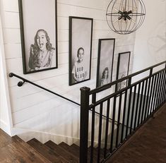 black and white photos hang on the wall next to an iron hand rail in front of a staircase