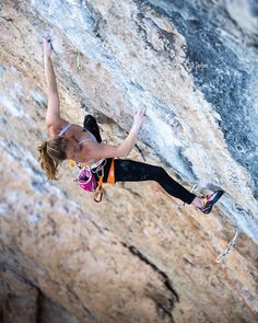 a woman climbing up the side of a mountain with her hands in the air while holding onto a rope