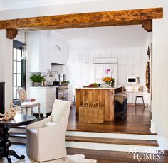 an open concept living and dining room with wood beams in the ceiling, hardwood floors, white chairs