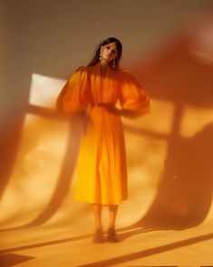 a woman in an orange dress standing next to a white wall with shadows on it