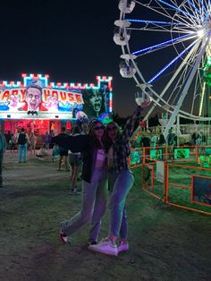 two young women standing in front of a ferris wheel at an amusement park with lights on