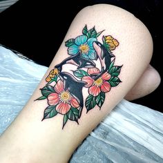 a close up of a person's leg with flowers on it and an orca in the background