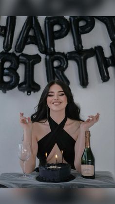 a woman sitting in front of a cake with candles on it and a bottle of wine next to her