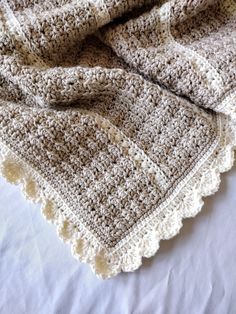 a crocheted blanket laying on top of a bed next to a white pillow