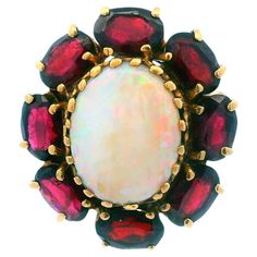 This beautiful opal and red garnet ring is a 1950's design. The ring is 14 karat yellow gold with a white opal centerpiece (12.75x9.55mm opal). The opal has excellent bright red and green flashes with a smooth and even color play. Said opal is framed by 8 gorgeous natural red garnets that flawlessly complement the yellow gold and the flashing colors of the opal. This ring is a size 7 but can easily be resized up or down! 14K Yellow Gold Opal & Garnet Cocktail Ring Ca. 1950s  Size 7 (Can be resiz Red Garnet Ring, 1950s Design, Color Play, Garnet Ring, Garnet Rings, White Opal, Red Garnet, Natural Red, Cocktail Ring