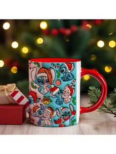 a red and white coffee mug sitting on top of a table next to a christmas tree