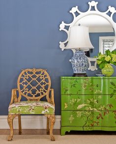 a blue and white room with a green dresser, mirror and lamp on the wall