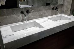 two sinks with faucets running from them in a public restroom, one is white and the other is black