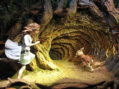 a woman and her dog are walking through a tunnel in the woods with fake trees