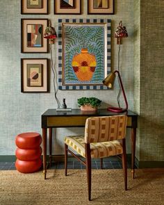 a desk with a chair, lamp and pictures on the wall above it in a living room