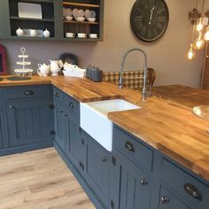 a kitchen with blue cabinets and wooden counter tops, an island sink and a large clock on the wall