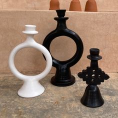 three black and white vases sitting next to each other on a counter top in front of a wall