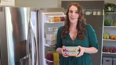 a woman standing in front of an open refrigerator holding a box of fruit and juice