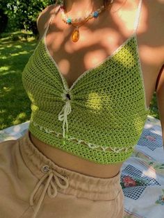 a woman wearing a green crochet top and tan shorts on a picnic table