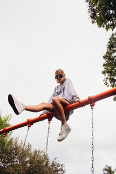 a woman sitting on top of a red metal pole with chains hanging from it's sides