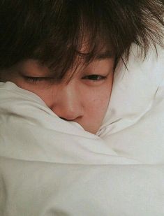 a young man sleeping under a blanket on top of a bed