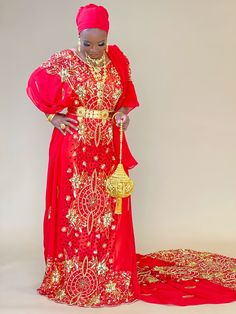 an african woman in a red and gold dress standing next to a large golden object