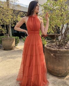 a woman in an orange dress standing next to a potted plant and looking up at the sky