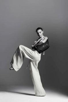 a woman is posing with her legs in the air while holding a handbag and wearing high heels