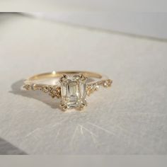 an engagement ring with a green emerald surrounded by small white and yellow diamonds on a sheet of paper