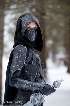 a man dressed in black with a hood and gloves on holding a snowboard while standing in the snow