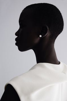 a woman with short black hair wearing a white top and earring on her head