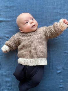 a baby laying on its back wearing a sweater and pants with one hand in the air