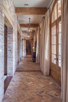 a long hallway with brick walls and wooden doors, windows, and curtains on either side