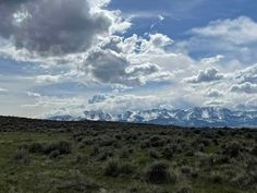 a field with mountains in the distance and clouds above it, on a cloudy day