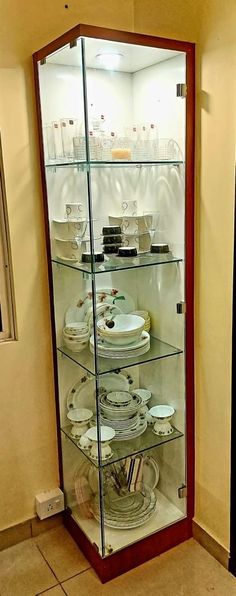 a glass display case filled with plates and bowls on top of a tiled floor next to a wall