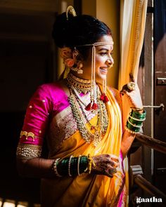 a woman in an orange and yellow sari with jewelry on her head standing next to a window