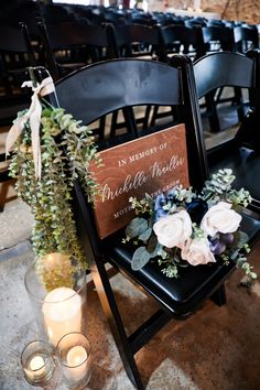 a wooden sign sitting on top of a black chair next to some flowers and candles