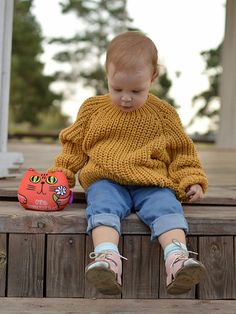 a small child sitting on top of a wooden bench next to a toy cat and an orange ball