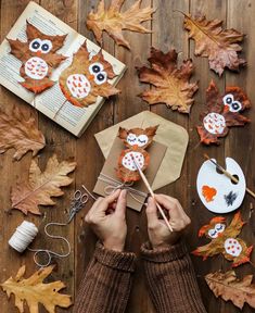 someone is making an owl craft out of leaves and other autumn decorations on a wooden table