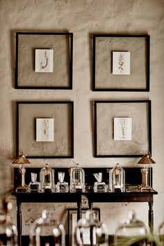 three framed pictures hang on the wall above a table with glass jars and vases