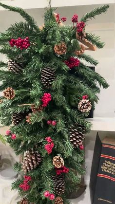 a christmas tree with pine cones and red berries on it next to an old book