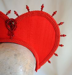 This striking headdress will take any Queen themed costume to another level! Queen of Hearts to Evil Queen, you will certainly won't pass unnoticed! The heart shape of this headpiece frames the face ever so elegantly giving the illusion of a heart. This piece is covered with silk shantung.It is embellished with crystals all around for that so in-fashion halo effect, as well as a beautiful inverted tear-drop focal element and finished off with braided trimming. Choose between red (pictured) or bl Queen Of Hearts Accessories Diy, Queen Of Hearts Crown Headband, Queen Of Hearts Wigs, Queen Of Hearts Neck Collar Diy, Queen Of Hearts Mannequin Head, Queen Of Hearts Costume, Dark Queen, Red Pictures, Costume Hats