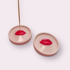 two pink bowls with red lipstick on them and a toothpick sticking out of one