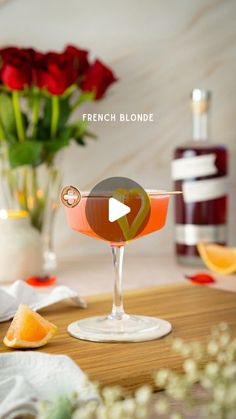 an orange and red drink sitting on top of a wooden table next to some flowers