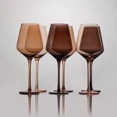 three different colored wine glasses sitting next to each other on top of a reflective surface