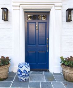 a blue and white vase sitting in front of a door with two planters next to it